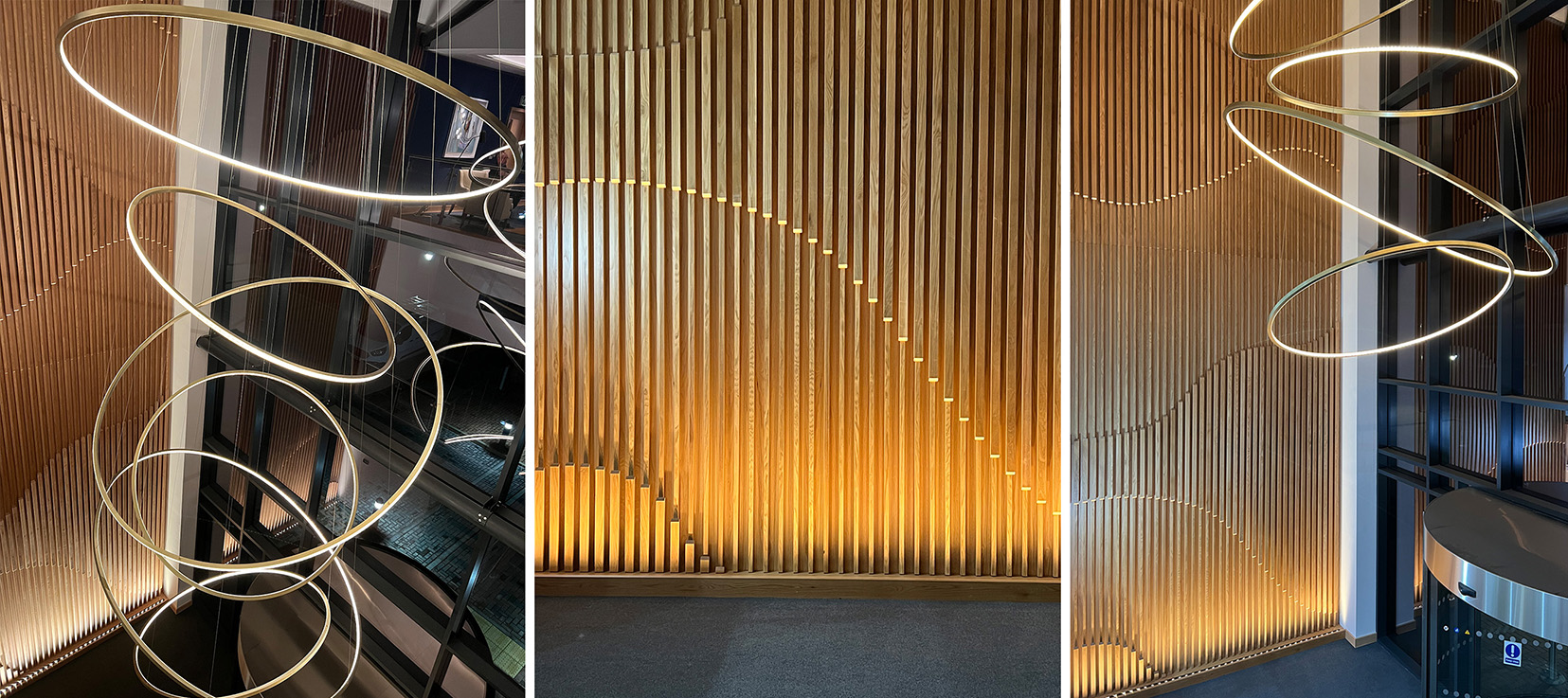 Office atrium with long circular pendant and uplit slated wooden wall