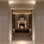 a wonderful corridor with uplights framing the door with a fireplace beyond in the centre with downlit niches either side
