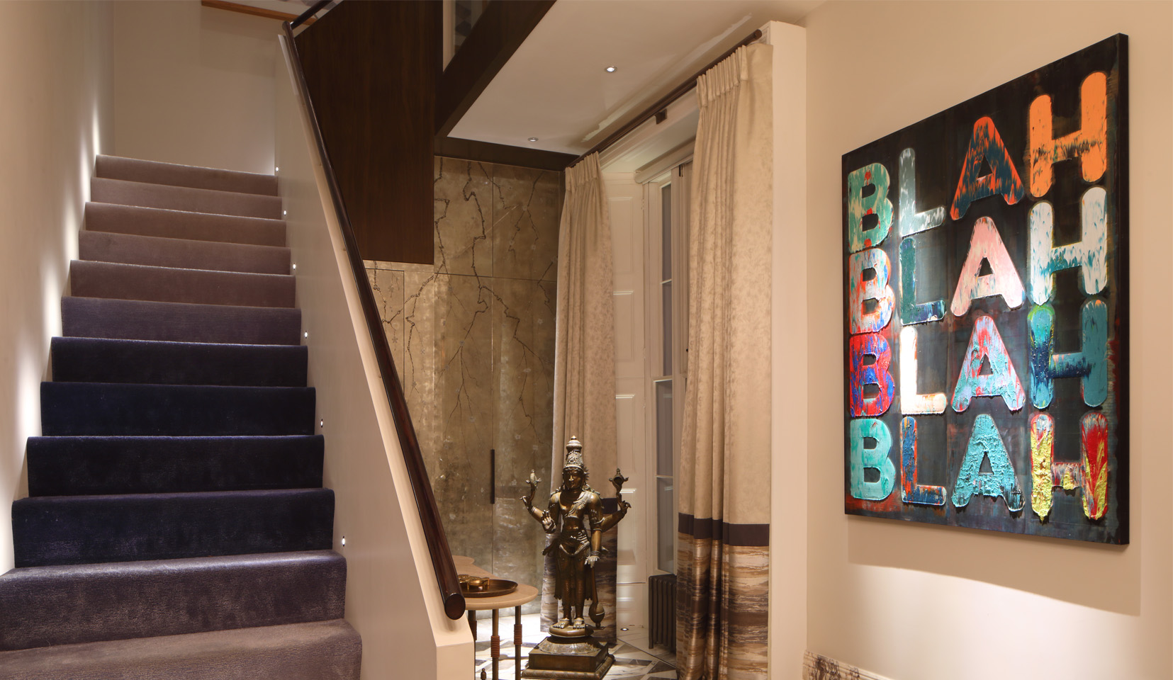 Hallway with large wall art lit with downlight and blue carpeted staircase lit with step lights