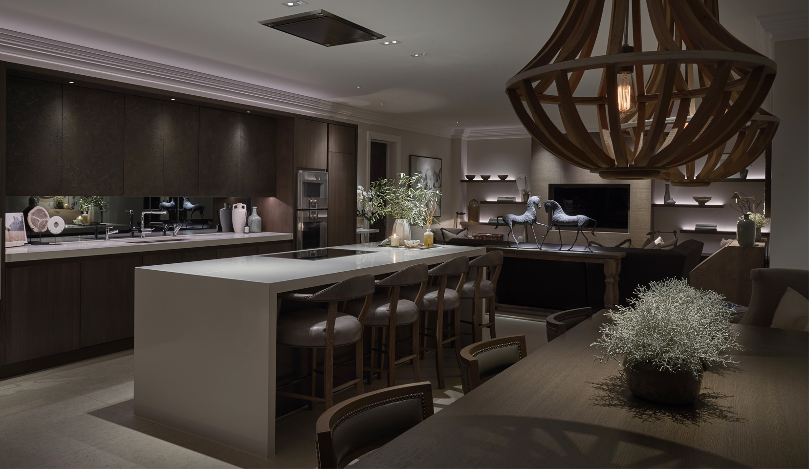 kitchen and seating area with oversized wooden pendants and downlights onto kitchen island, with lit shelves in background