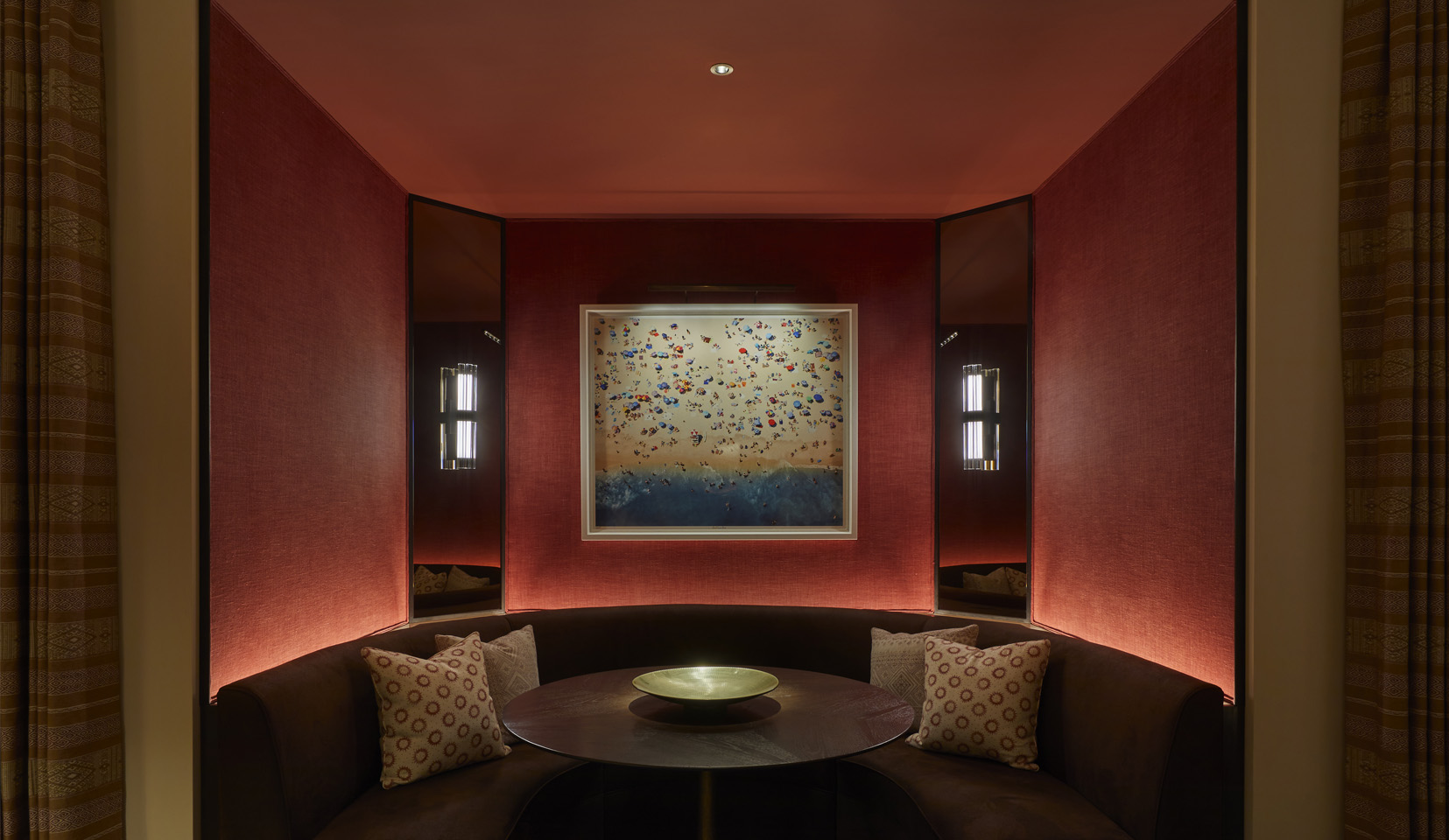 Red walled booth seating area with picture light above painting