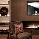 close up detail of backlit shelving with books and objects with armchair and fireplace
