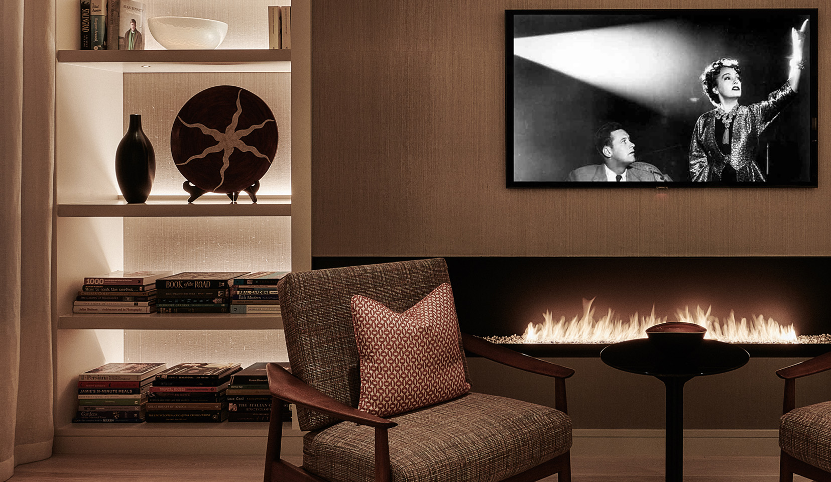 close up detail of backlit shelving with books and objects with armchair and fireplace