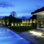 Swimming pool surrounded by lit trees and a glass extension with light underneath